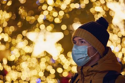 Close-up of man wearing mask against illuminated christmas tree during winter