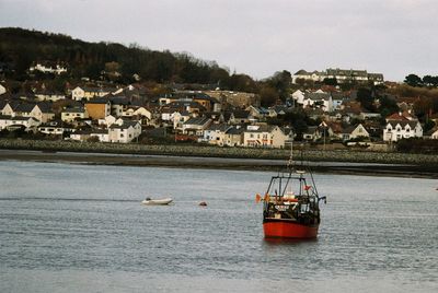 Sailboats in sea by townscape against sky