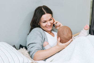 Mother speaking on mobile phone with cute baby boy on bed, natural tones, love emotion
