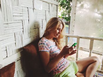 Woman using smart phone while sitting at porch