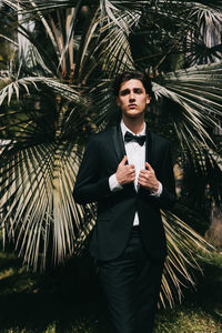 A beautiful young man, the groom in an elegant wedding suit, stands posing in the city's old park