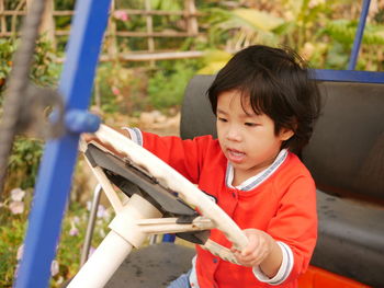 Asian baby girl, 3 years old, holding on a steering wheel and pretending to drive a parking car 