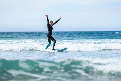 Full length of woman with arm raised surfing in sea against clear sky
