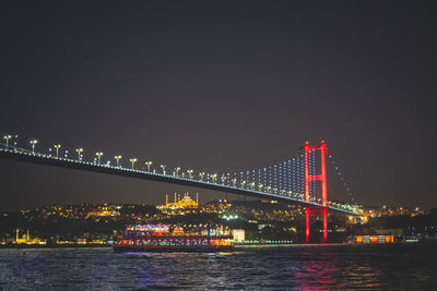Illuminated bridge over river in city against clear sky at night