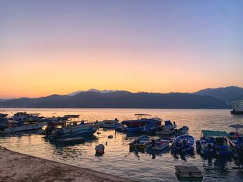 Boats moored in harbor at sunset