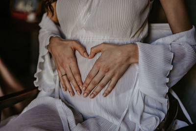 Midsection of woman making heart shape on abdomen