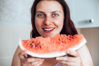 Portrait of smiling woman holding watermelon at home
