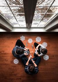 Woman and two boys sitting on floor cutting paper snowflakes. .