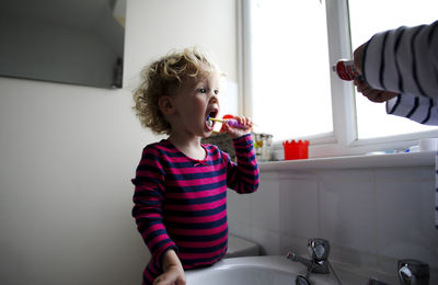 Cropped hands of brother holding toothpaste while sister brushing
