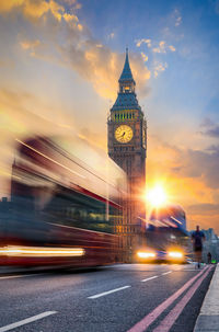 Illuminated clock tower against sky in city during sunset