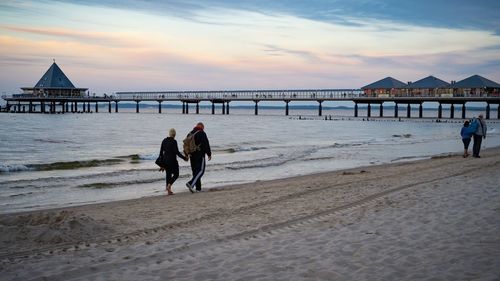 Rear view of people walking on beach against sky during sunset