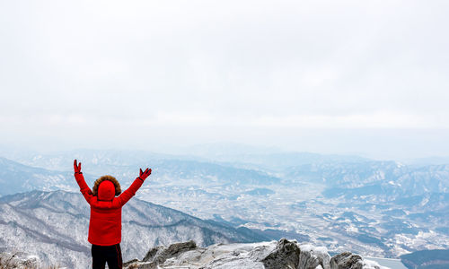 Rear view of person with arms raised standing on mountain against sky