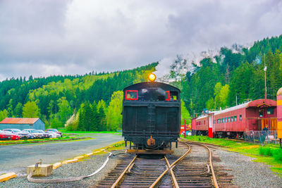 Trains on railroad track against cloudy sky