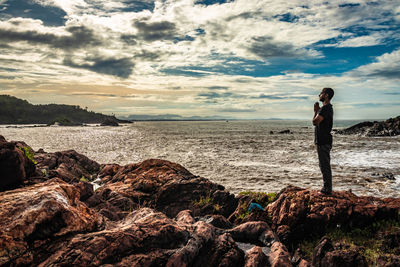 Site view of man standing on rock by sea against sky