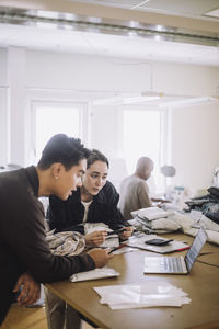 Male and female design professional watching laptop while leaning on workbench at workshop