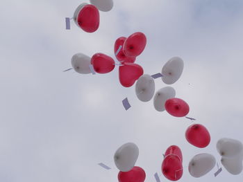 Low angle view of heart shape balloons with label flying against sky