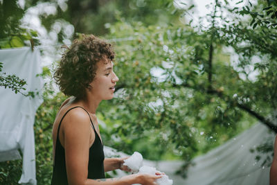 Side view of young woman standing against plants