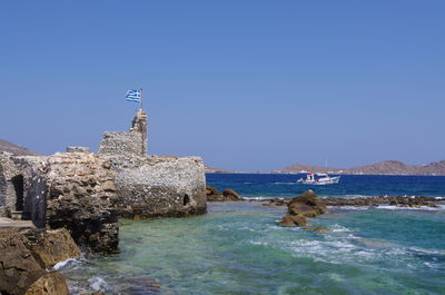 Sea by rocks against clear blue sky