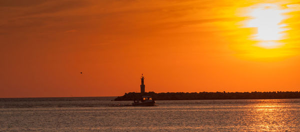 Silhouette ship in sea against orange sky