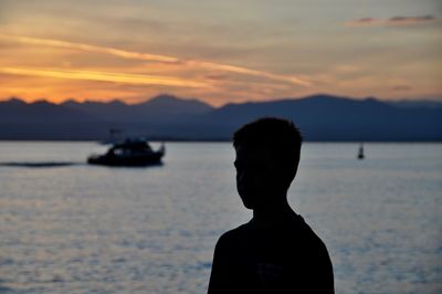 Rear view of silhouette man on boat in sea against sunset sky