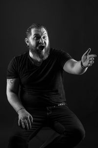 Portrait of man sitting against black background