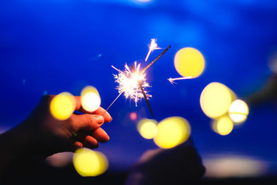 Cropped image of hands holding sparkler against sky at night