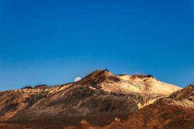 Panoramic view of etna volcano against the clear blue sky of sunrise and the setting moon behind