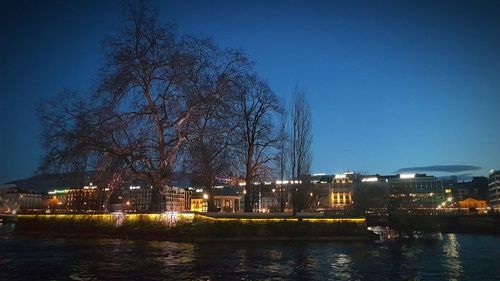 River by illuminated city against clear blue sky at night