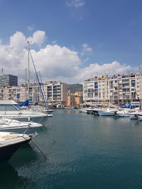 Sailboats moored in harbor by buildings against sky