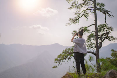 Rear view of man standing on mountain against sky during sunset