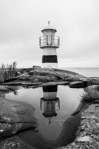 Lighthouse with reflection at beach against sky