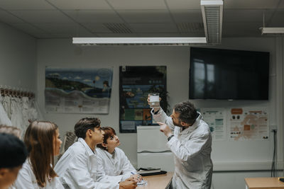 Male professor examining chemical in beaker while explaining to student at science lab