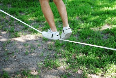 Low section of man walking on tightrope over field