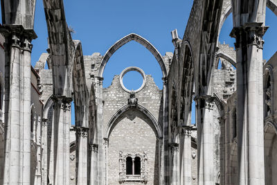 Low angle view of cross amidst buildings against sky