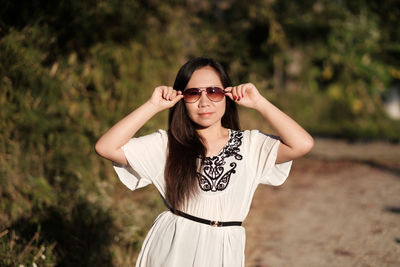 Portrait of smiling young woman wearing sunglasses standing against trees