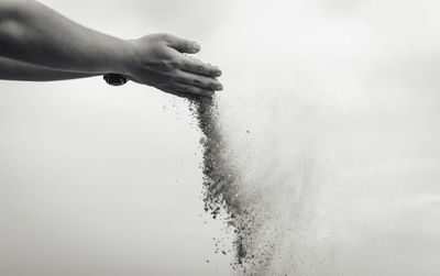 Cropped hand sprinkling sand against sky