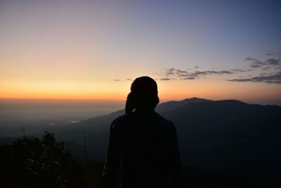 Rear view of silhouette man standing on mountain against sky during sunset