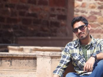 Handsome young man wearing sunglasses sitting on retaining wall