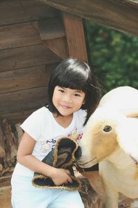 Portrait of cute smiling girl standing by artificial sheep