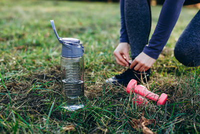 Fitness in the park, girl tying the shoe, foot bottle and dumbbells, close up.