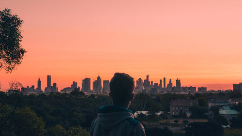 Rear view of man and buildings against sky during sunset