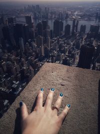 Cropped hand of woman on retaining wall with cityscape in background