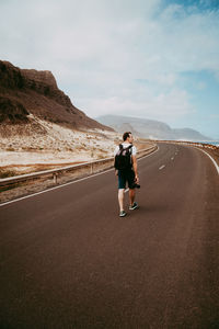 Rear view of man walking on road against sky