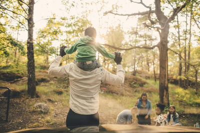 Man carrying son shoulders during picnic with family in public park