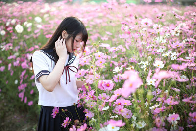 Side view of young woman standing amidst flowering plants