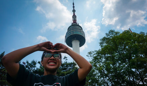 Smiling woman making heart shape against tower in city