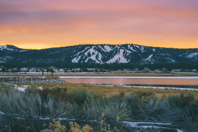 Scenic view of lake amd snowcapped mountains against cloudy sky during sunset