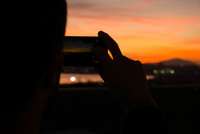 Silhouette man holding camera against sky during sunset