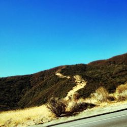 Road leading towards mountains against clear blue sky