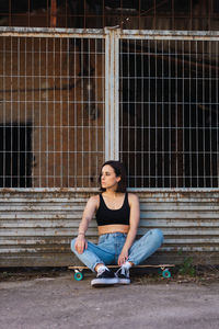 Woman with skateboard sitting by fence